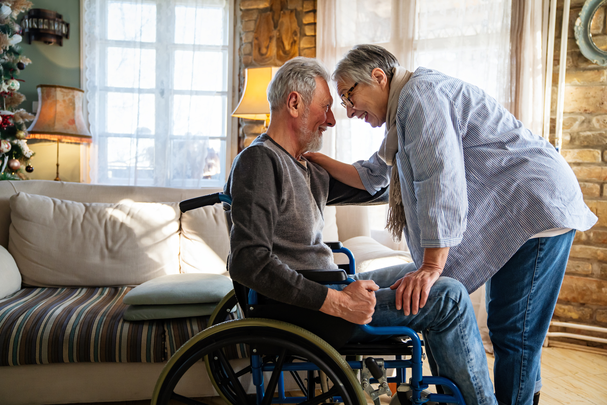 Romantic happy senior couple in love at home. Mature man with disability in wheelchair having fun with wife